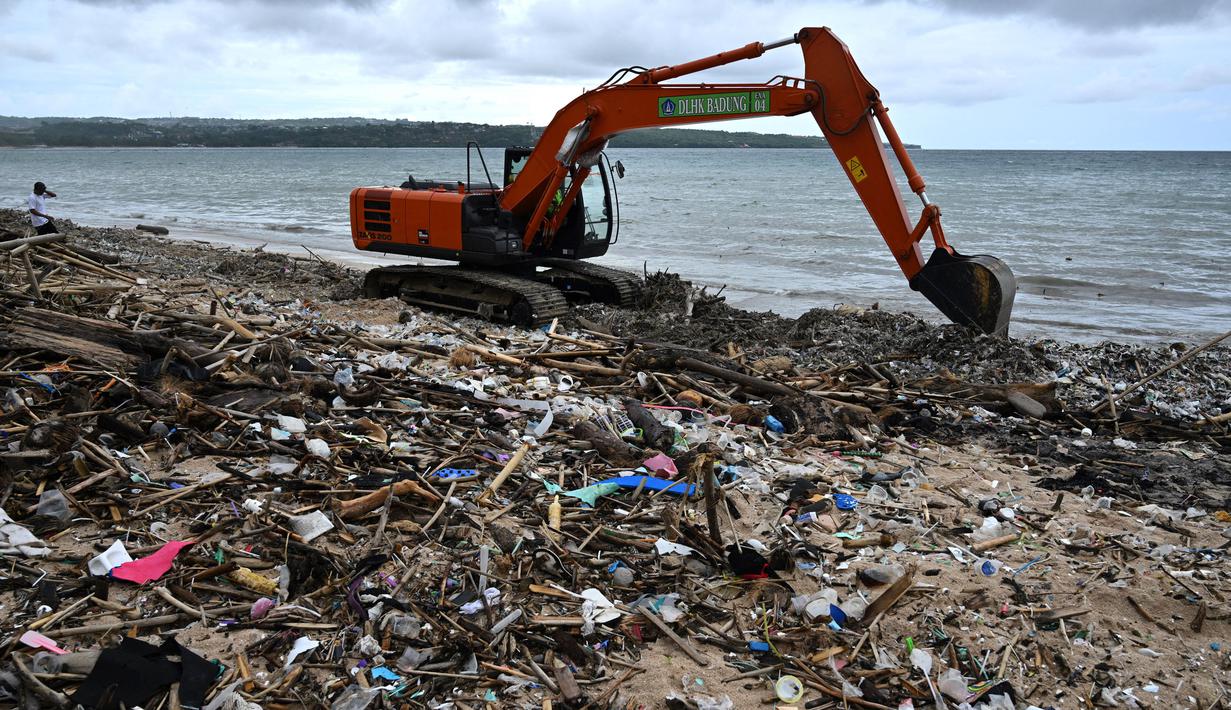 Para pekerja menggunakan alat berat jenis excavator membersihkan sampah yang terdampar dan menumpuk di sebuah pantai di Kedonganan, Kabupaten Badung, Bali pada Jumat 3 Januari 2025. (SONNY TUMBELAKA/AFP)