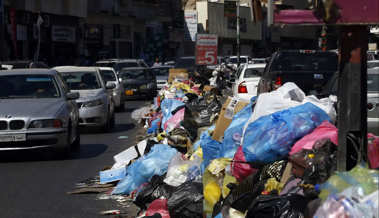 Kendaraan melintas di samping tumpukan sampah di sepanjang sisi jalan di Tripoli, ibukota Libya (30/9/2019). Berton-ton sampah berserakan dari tempat sampah dan menumpuk di pinggir jalan. (AFP Photo/Mahmud Turkia)