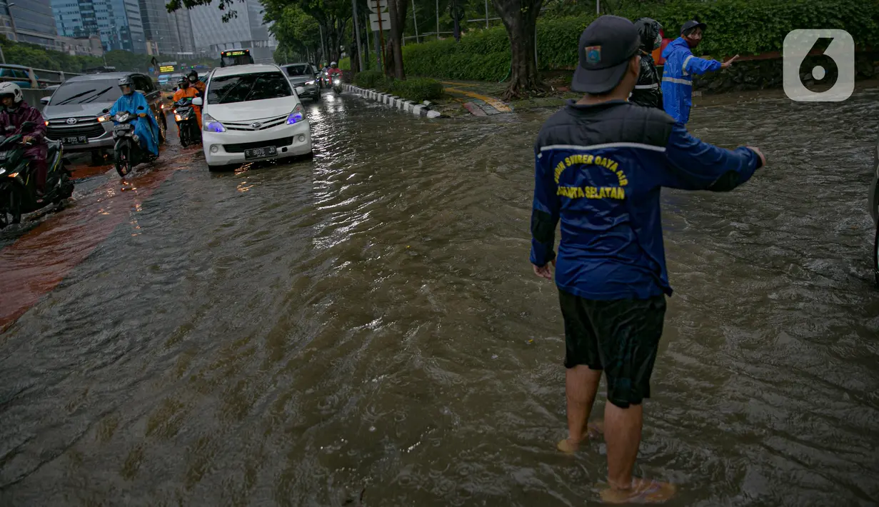 Petugas mengatur kelancaran lalu lintas saat air menggenangi ruas Jalan Gatot Subroto, Jakarta, Kamis (18/2/2021). Hujan deras yang mengguyur wilayah Jakarta menyebabkan terjadinya genangan di beberapa ruas jalan, meski begitu sejauh ini kendaraan masih dapat melintas. (Liputan6.com/Faizal Fanani)