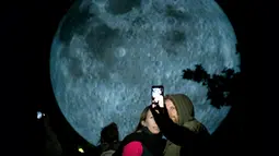 Pengunjung berswafoto dengan latar belakang replika bulan raksasa yang dipajang di Bratislava, Slovakia, 7 Oktober 2017. Replika bulan tersebut merupakan karya seniman Inggris, Luke Jerram yang bertajuk 'Museum of The Moon'. (JOE KLAMAR / AFP PHOTO)