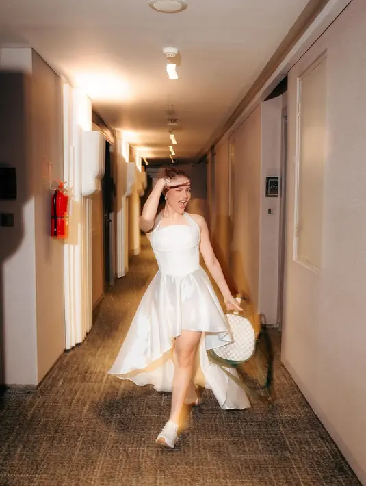 Ia mengenakan dress putih karya @yoss_bridal_couture yang menghadirkan siluet anggun nan elegan. Potongan halter-neck pada dress memberi kesan modern sekaligus fresh, cocok untuk acara spesial namun tetap terasa effortless.   [@davinaakaramoy].