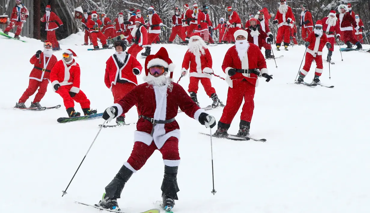 Pemain ski dan snowboarder berpakaian Santa Claus menuruni lereng gunung saat Santa Sunday ke-19 di Newry, Maine, AS, Minggu (2/12). Lebih dari 200 Santa menuruni lereng gunung secara massal dalam acara Santa Sunday tahun ini. (AP Photo/Robert F. Bukaty)