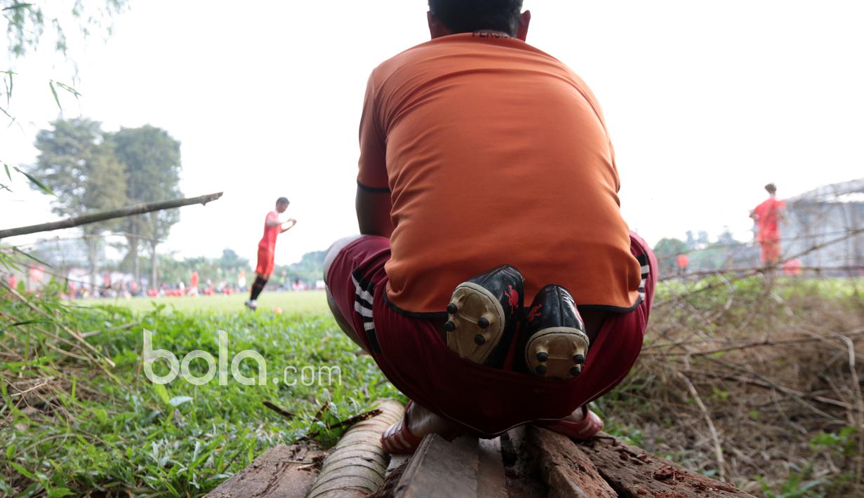 Seorang penonton menyelipkan sepatu bola dicelana saat menyaksikan sesi latihan Persija Jakarta di Lapangan POR Sawangan, Sabtu (21/1/2017). (Bola.com/Nicklas Hanoatubun)