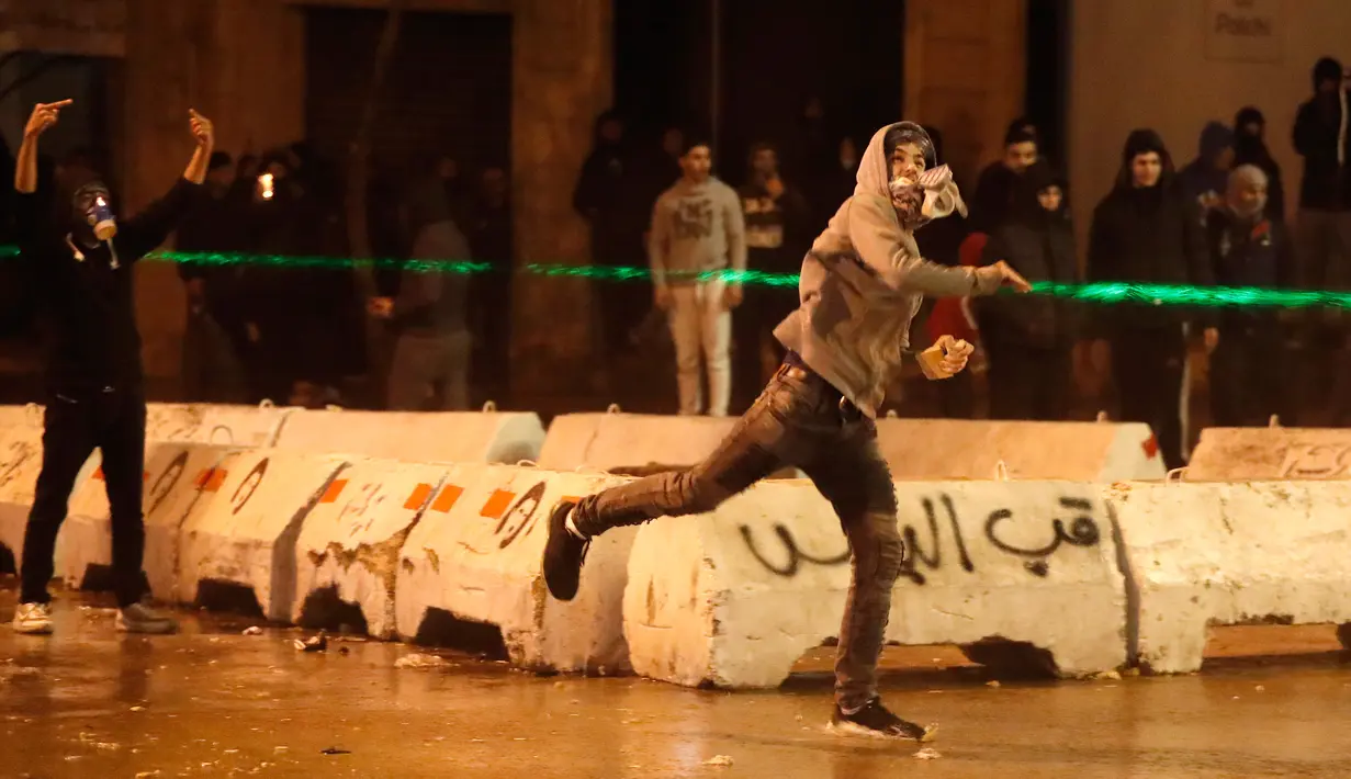 Demonstran antipemerintah melemparkan batu ke arah polisi antihuru-hara saat demonstrasi menentang pemerintahan baru dekat Parliament Square, Beirut, Lebanon, Rabu (22/1/2020). Demonstrasi dan kekerasan terus berlanjut kendati Lebanon telah mengumumkan kabinet baru. (AP Photo/Hussein Malla)