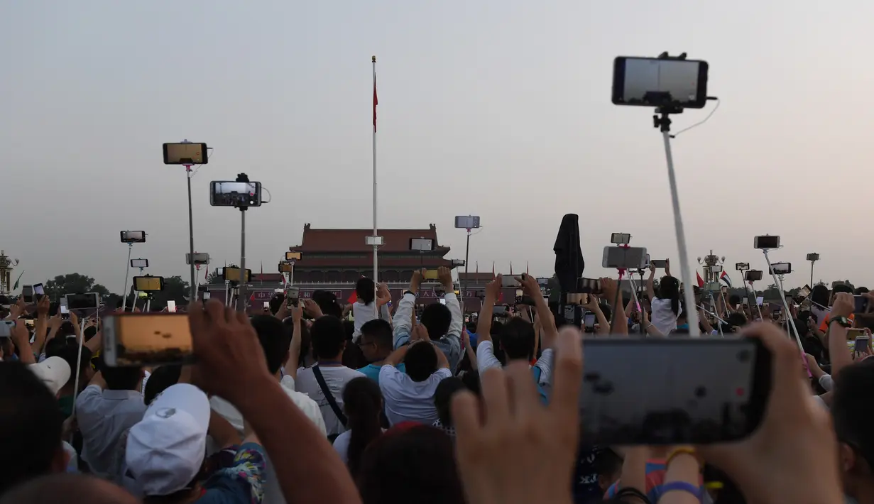 Warga mengambil foto setelah upacara pengibaran bendera saat fajar setelah kematian mantan perdana menteri China Li Peng di Lapangan Tiananmen Beijing (24/7/2019). Li Peng biasa dikenal sebagai "Jagal Beijing" meninggal di usia 90 tahun. (AFP Photo/Greg Baker)