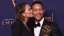 Chrissy Teigen mencium John Legend selama Creative Arts Emmy 2018 di Microsoft Theater di Los Angeles, California, AS (9/9). Penghargaan ini untuk artis yang telah memenangkan di Emmy, Grammy, Oscar, dan Tonys. (AFP Photo/Alberto E. Rodriguez)