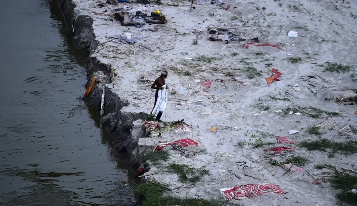 Seorang pria berjalan di tengah kuburan dangkal di pasir, beberapa di antaranya diduga orang yang meninggal karena virus corona COVID-19, dekat tempat kremasi di tepi Sungai Gangga, Phafamau, Allahabad, India, Sabtu (5/6/2021). (SANJAY KANOJIA/AFP)