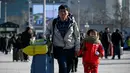 Seorang pria menggandeng bocah sambil membawa koper berjalan ke pintu masuk stasiun kereta api Beijing, Jumat (10/1/2020). Puluhan ribu warga China telah meninggalkan kota-kota besar China menuju kampung halaman, guna merayakan Tahun Baru Imlek pada 25 Januari mendatang. (WANG ZHAO/AFP)