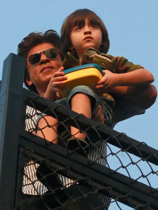 Aktor Bollywood, Shahrukh Khan sambil menggendong putranya, AbRam menyapa para fans yang berkumpul di depan rumahnya di Mumbai, India, Kamis (2/11). Pria yang sering dipanggil SRK ini berulang tahun yang ke 52. (AP Photo/Rafiq Maqbool)