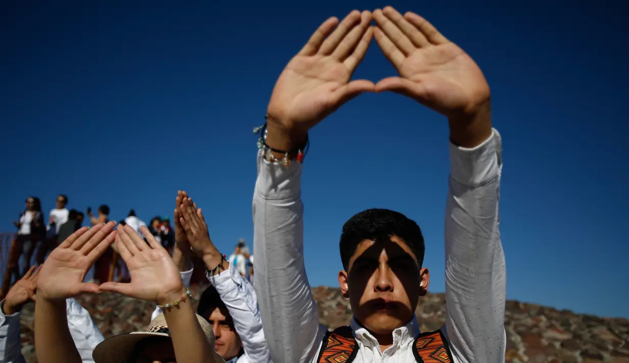 Pengunjung mengangkat tangan mereka yang membentuk segitiga saat merayakan equinox musim semi di situs arkeologi Teotihuacan, Meksiko (21/3). Tradisi Equinox ditandai dengan posisi matahari yang bersinar vertikal. (AP Photo/Rebecca Blackwell)
