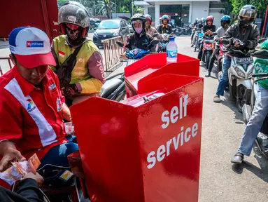Seorang pekerja SPBU (kiri) menerima pembayaran dari pengendara yang mengantre untuk mengisi bahan bakar sepeda motor mereka di sebuah Stasiun Pengisian Bahan Bakar Umum (SPBU), Jakarta pada Rabu 1 April 2026. Pemerintah resmi tidak mengubah harga Bahan Bakar Minyak (BBM) di dalam negeri, baik harga BBM subsidi maupun non subsidi. (BAY ISMOYO/AFP)