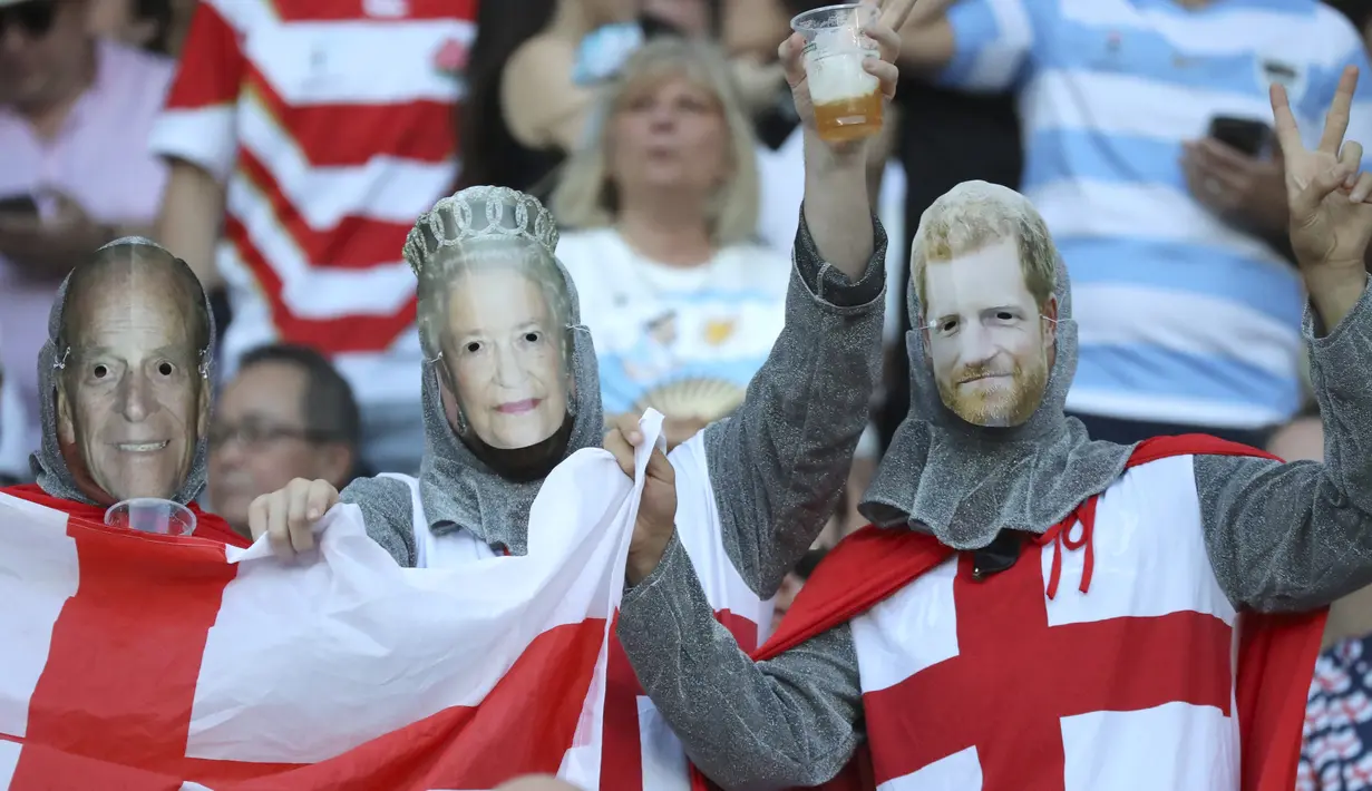 Fans Inggris mengenakan topeng Pangeran Harry, Ratu Elizabeth II dan suaminya Philip Mountbatten sebelum pertandingan antara Inggris dan Argentina di Tokyo, Jepang (5/10/2019). (AP Photo/Eugene Hoshiko)