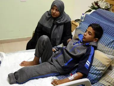 Seorang bocah Palestina, Adel Rahman Nawfal (12) berbaring di ranjang rumah sakit ditemani neneknya di kota Ramallah, Tepi Barat, Senin (23/4). Nawfal kehilangan satu kakinya akibat terkena tembakan oleh pasukan Israel. (AFP/ABBAS MOMANI)
