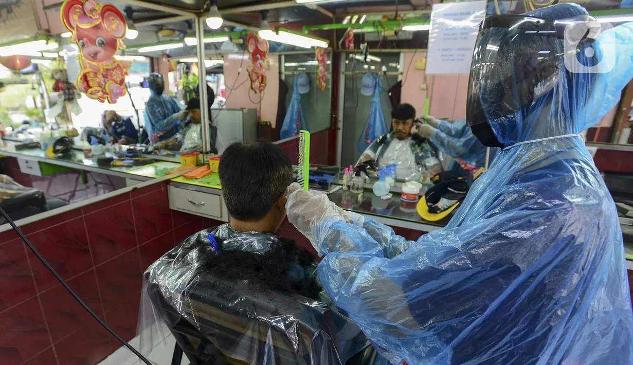 Tukang cukur mengenakan alat pelindung diri (APD) dari plastik saat mencukur rambut pelanggan di Pondok Kelapa, Jakarta, Selasa (5/5/2020). Tukang cukur mengenakan APD untuk mengurangi risiko penularan virus corona COVID-19. (merdeka.com/Imam Buhori)