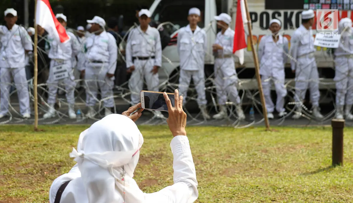 Seorang wanita mengambil gambar Massa Forum Umat Islam yang mengikuti 'Apel Siaga Umat untuk Pemilu Bersih, Jujur, dan Adil' di depan Kantor KPU, Jakarta, Minggu (31/3). Massa menolak segala bentuk kecurangan dalam Pemilu yang akan berlangsung 17 April mendatang. (Liputan6.com/Immanuel Antonius)