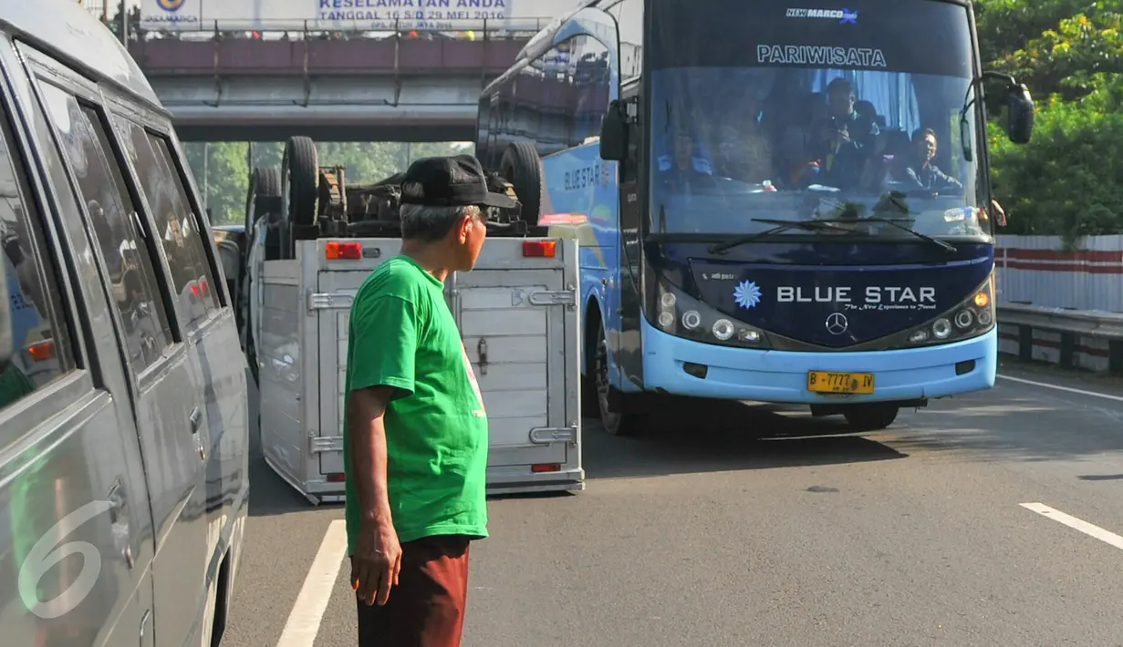 Bus pariwisata berjalan melewati mobil boks yang terbalik di KM 02 Tol Cawang arah Cililitan, Jakarta, Senin (30/5). Petugas tengah melakukan penyelamatan pengemudi dan membawa badan mobil bernomor polisi B 9385 HH itu (Liputan6.com/Yoppy Renato)