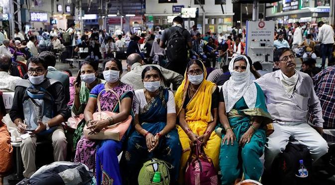 Orang India yang menunggu di stasiun kereta api memakai masker pelindung sebagai tindakan pencegahan terhadap pandemi Virus Corona. (Rajanish Kakade / AP Photo]