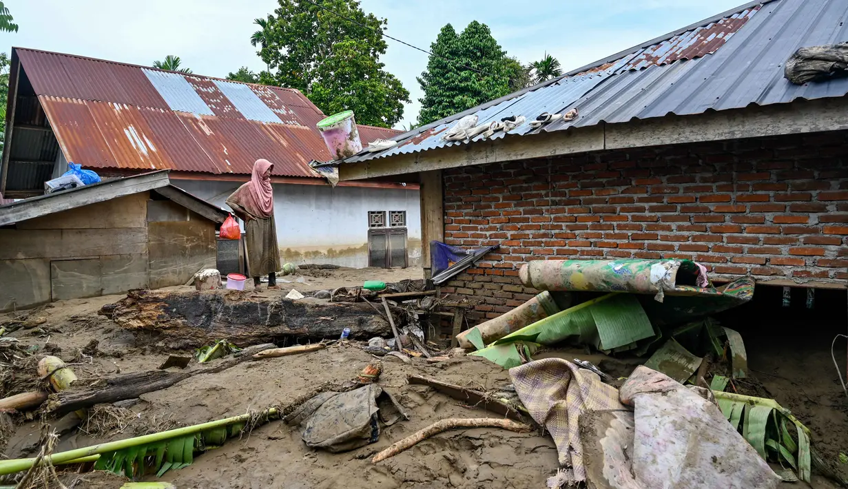 Sebelumnya, hujan deras yang mengguyur Aceh selama sepekan terakhir menyebabkan banjir parah di sejumlah kabupaten. Tampak dalam foto, warga berdiri di atas lumpur tebal di dekat rumahnya yang terendam banjir bandang di Meureudu, Kabupaten Pidie Jaya, Provinsi Aceh, Jumat 28 November 2025. (CHAIDEER MAHYUDDIN/AFP)