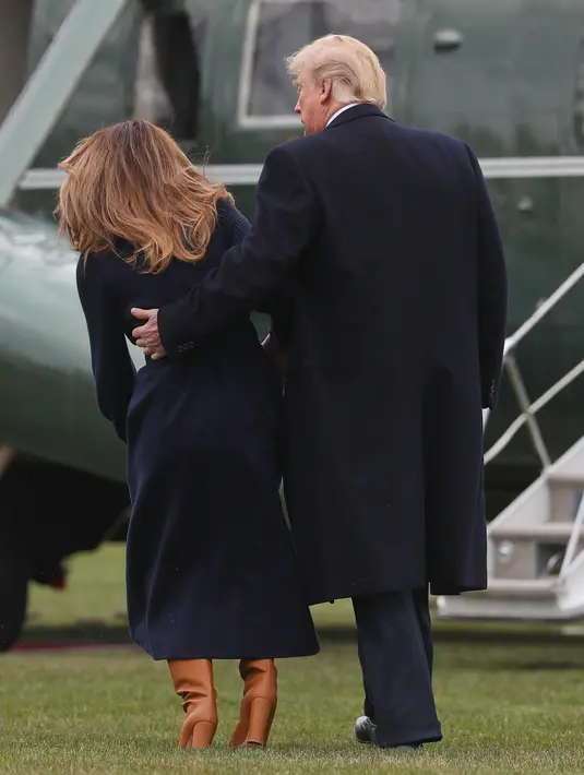 Presiden AS Donald Trump merangkul Melania Trump yang hampir terjatuh saat berjalan menuju helikopter kepresidenan di Gedung Putih, Senin (19/3). Melania Trump kehilangan keseimbangan saat mengenakan sepatu berhak 10 cm itu.  (AP/Pablo Martinez Monsivais)