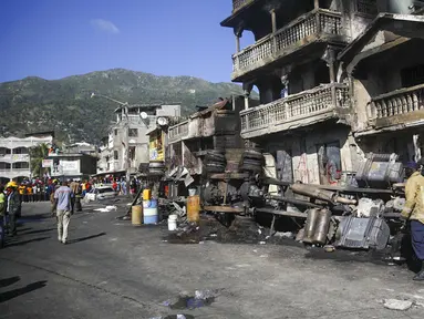 Petugas pemadam kebakaran berdiri dekat bangkai truk pengangkut BBM yang terbalik dan meledak di Cap-Haitien, Haiti, 14 Desember 2021. Ledakan tersebut menghanguskan mobil dan rumah serta menewaskan puluhan orang. (AP Photo/Joseph Odelyn)