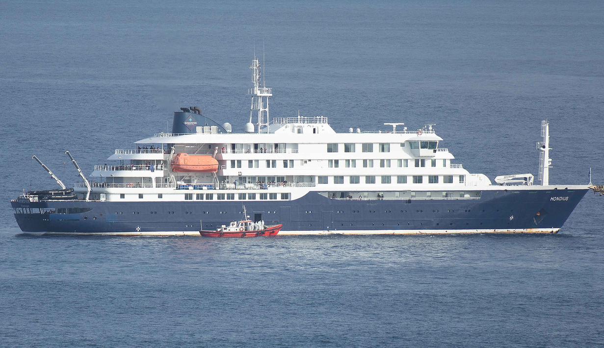 Tertahannya Kapal pesiar MV Hondius di lepas pantai Praia, Tanjung Verde, menyusul wabah mematikan Hantavirus yang terjadi. Tampak dalam foto, sebuah perahu ambulans yang membawa awak kapal yang mengenakan pakaian pelindung bahan berbahaya (hazmat suit) mendekati pintu kemudi di sisi kanan kapal pesiar MV Hondius, saat kapal tersebut berhenti di lepas pelabuhan Praia, ibu kota Tanjung Verde, pada Selasa 5 Mei 2026. (Foto oleh AFP)