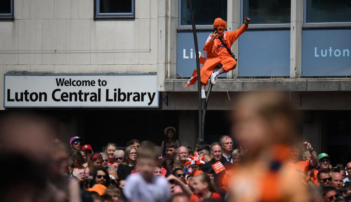 Seorang pendukung Luton Town menyambut kedatangan parade bus timnya melewati jalanan di Luton, Inggris setelah berhasil promosi ke Liga Inggris musim 2023/2024 pada Senin (29/05/2023) waktu setempat. The Hatters sukses menyegel tiket promosi setelah memenangkan laga play-off divisi Championship melawan Covetry City 6-5 melalui adu penalti di Wembley, Sabtu (27/5/2023). (AFP/Daniel Leal)
