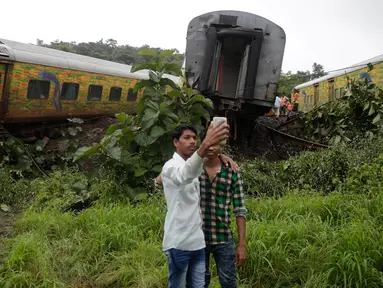 Dua remaja India berswafoto di dekat gerbon kereta yang tergelincir di Asangaon, India (29/8). Sebuah kereta penumpang mengalami kecelakaan di  sekitar 70 kilometer dari Mumbai. (AP Photo / Rafiq Maqbool)