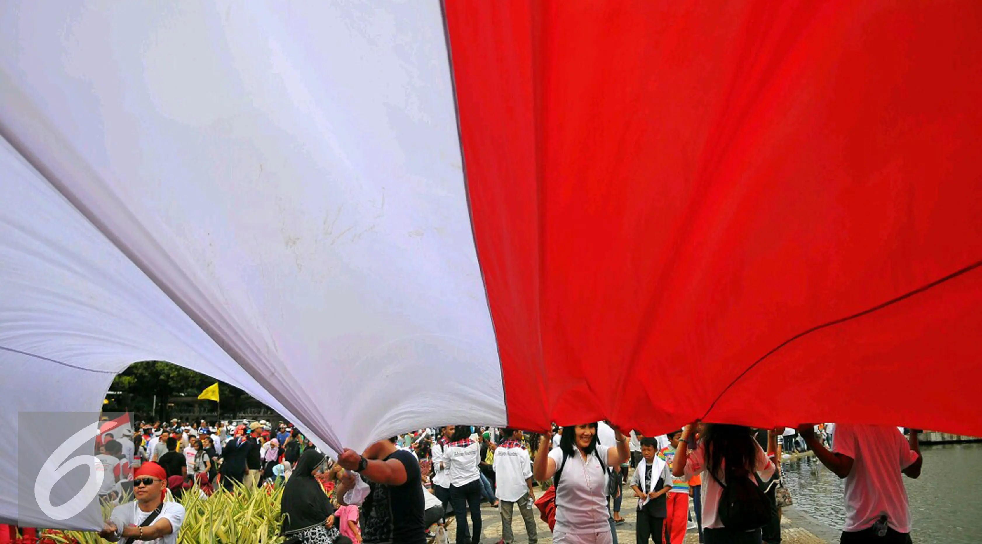 Seorang peserta 'Aksi Kita Indonesia' membentangkan Bendera Merah Putih raksasa di Bundaran HI, Jakarta, Minggu (4/12). Mereka juga membawa berkeliling Bendera Merah Putih raksasa sambil meneriakkan 'Kita Indonesia'. (Liputan6.com/Angga Yuniar)