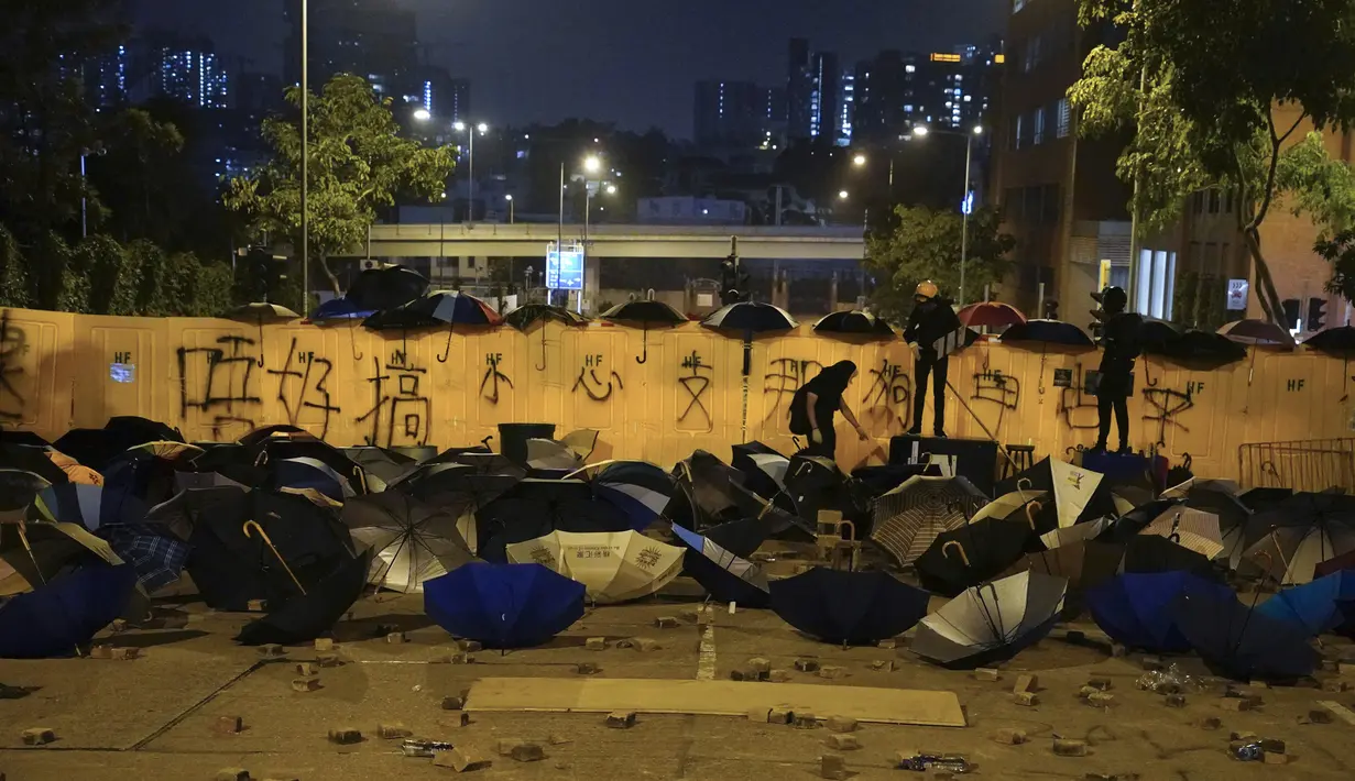 Para pengunjuk rasa pro-demokrasi menghalangi jalan yang berhamburan dengan payung dan batu bata di luar kampus Universitas Baptis Hong Kong di Hong Kong (13/11/2019). (AP Photo/Vincent Yu)