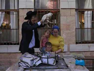 Seorang pria Yahudi ultraortodoks mengayunkan seekor ayam di atas kepala anggota keluarganya saat melakukan ritual Kapparot di Yerusalem, 13 September 2021. Kapparot adalah ritual transfer dosa ke ayam yang dilakukan sebelum Yom Kippur (Hari Penebusan). (MENAHEM KAHANA/AFP)
