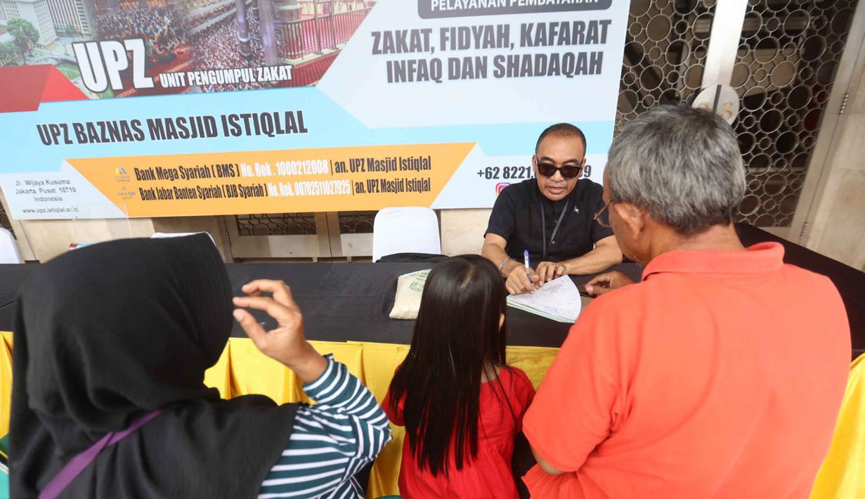 Petugas Unit Pengelola Zakat (UPZ) melayani pembayaran zakat, fidyah, kafarat, infaq, dan shadaqah di teras Masjid Istiqlal, Jakarta, Minggu 15 Maret 2026. Selain menjalankan ibadah selama bulan suci Ramadan, umat muslim juga diwajibkan untuk menunaikan zakat fitrah. (Kapanlagi.com/Budy Santoso)