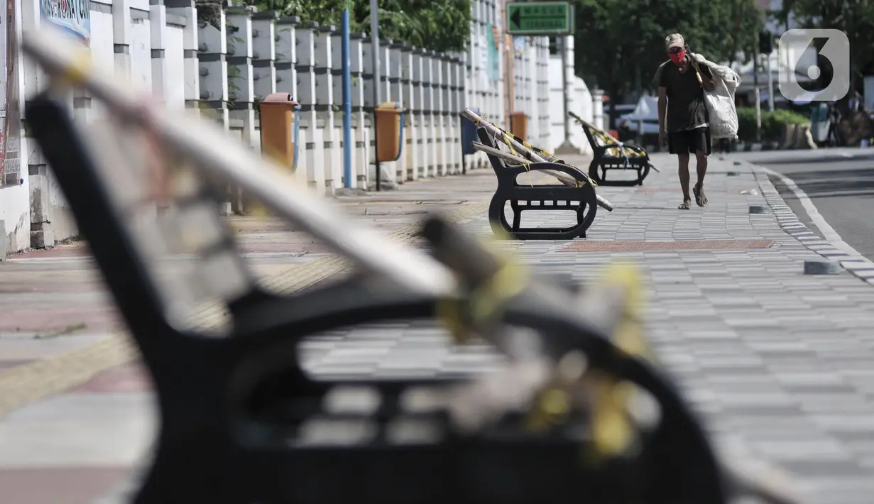 Pemulung melintasi deretan bangku trotoar yang disegel garis pembatas dan ditutupi bambu, Rawamangun, Jakarta, Minggu (3/5/2020). Bangku trotoar di sepanjang jalan Rawamangun disegel untuk mencegah kerumunan warga sebagai upaya memutus rantai penyebaran COVID-19. (merdeka.com/Iqbal S. Nugroho)
