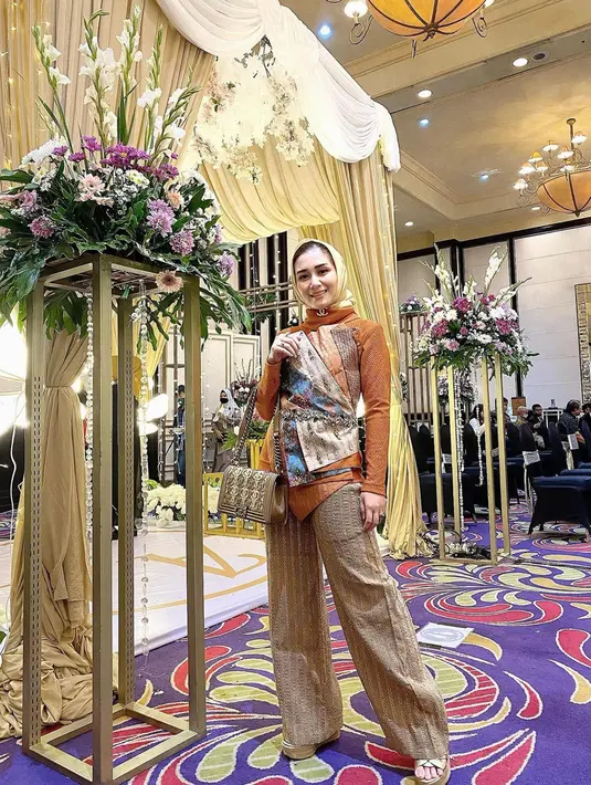 Tidak hanya menawan dengan gaun, Dine Mutiara juga tampil stunning saat mengenakan busana kondangan dengan setelan celana panjang. Baju yang dikenakannya juga semakin elegan dengan tambahan kain etnik yang berlapis-lapis. Sebagai pelengkap penampilan, Dine memilih tas yang warnanya senada dengan celana. (Liputan6.com/IG/@dine.pearl)