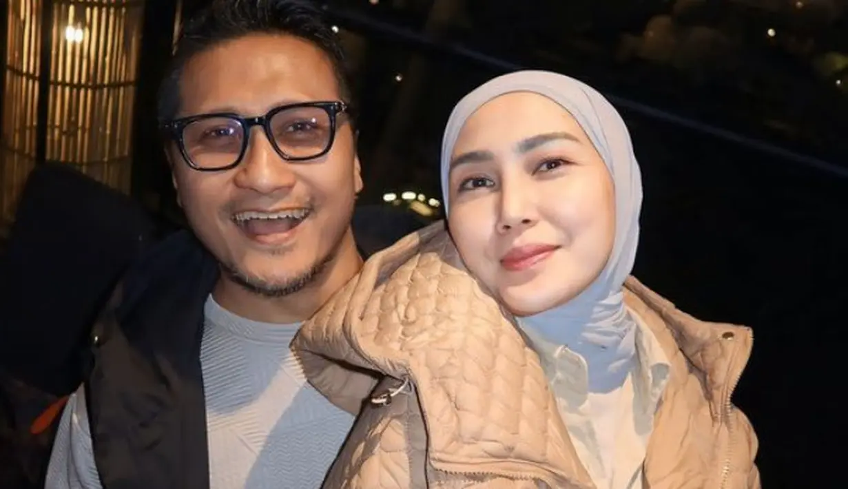 Fenita Arie mengenakan jaket puff coklat muda dipadukan inner kemeja dan kerudung abu-abu. Arie Untung mengenakan vest hitam dipadukan kaos abu-abu. [@ryana_dea]