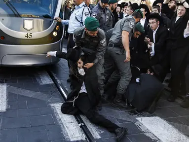 Pasukan keamanan Israel saling tarik-menarik dengan demonstran Yahudi Ultra-Ortodoks yang memblokir jalan utama saat melakukan aksi menentang wajib militer Israel di Yerusalem (17/10). (AFP Photo/Menahem Kahana)