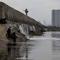 Namun, kali ini, Banjir rob di kawasan Muara Baru Jakarta diperparah dengan kebocoran dan rembesan pada tanggul laut di beberapa titik di Muara Baru, yang disebabkan oleh usia tanggul yang sudah tua dan korosi. Tampak dalam foto, seorang pria dengan pancingnya berjalan di atas tanggul laut raksasa yang dibangun untuk mencegah banjir di pesisir utara, seperti terlihat di Muara Baru, Jakarta pada Sabtu 6 Desember 2025. (ADITYA IRAWAN/AFP)