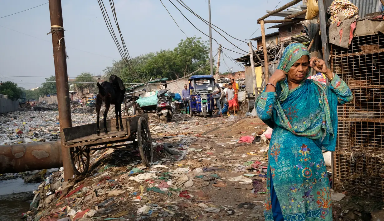 Seorang wanita marapikan kain dikepalanya ketika dia berjalan di dekat saluran pembuangan air limbah yang dipenuhi sampah di lingkungan berpenghasilan rendah di New Delhi, India (4/10/2019). (AFP Photo/Noemi Cassanelli)