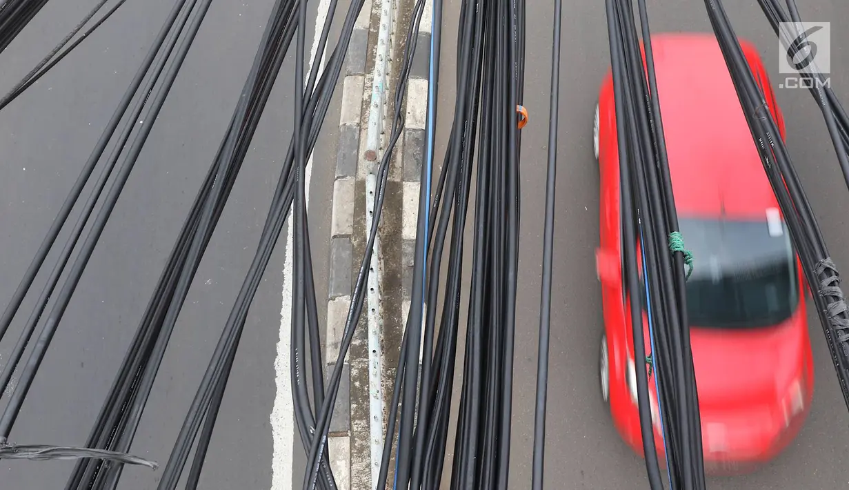 Instalasi kabel semrawut menjuntai di Jalan Dewi Sartika, Jakarta Timur, Sabtu (19/1). Selain mengganggu keindahan kota, kondisi tersebut juga berbahaya karena dapat memicu hubungan pendek arus listrik. (Liputan6.com/Immanuel Antonius)