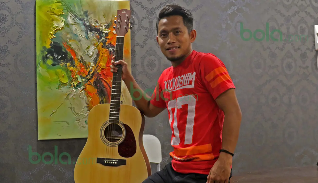 Andik Vermansah berpose dengan gitar miliknya dalam apartemen di kawasan Shah Alam, Selangor, Malaysia, Rabu (27/01/2016). (Bola.com/Nicklas Hanoatubun)