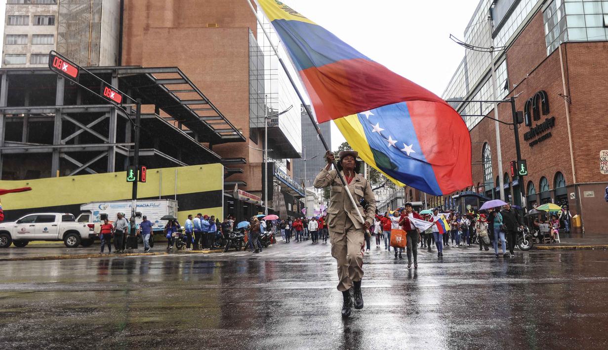 Seorang anggota milisi Venezuela memegang bendera nasional Venezuela selama pawai dukungan untuk mantan Presiden Venezuela Nicolas Maduro dalam sebuah unjuk rasa yang diselenggarakan oleh para pekerja di Caracas pada 14 Januari 2026. Pendukung pemerintah dan kelompok pro-Chavez turun ke jalan-jalan di Caracas, Venezuela, Rabu 14 Januari 2026. (Pedro MATTEY/AFP)
