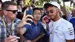 Pembalap Mercedes, Lewis Hamilton melakukan selfie dengan seorang penggemar menjelang sesi latihan bebas pertama di Grand Prix Australia, Melbourne, Jumat (24/3). (AFP Photo/WILLIAM WEST)