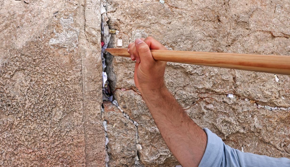 Pekerja dilengkapi dengan tongkat panjang membersihkan catatan yang dijejalkan di celah-celah Tembok Barat, tempat doa paling suci Yudaisme di Kota Tua Yerusalem pada 20 September 2022. (AFP/Ahmad Gharabli)
