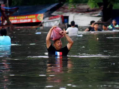 Warga melintasi banjir yang merendam perumahan Villa Mutiara Pluit, Tangerang, Banten, Senin (3/2/2020). Banjir disebabkan jebolnya tanggul sungai di sekitar kawasan tersebut. (merdeka.com/Magang/Muhammad Fayyadh)