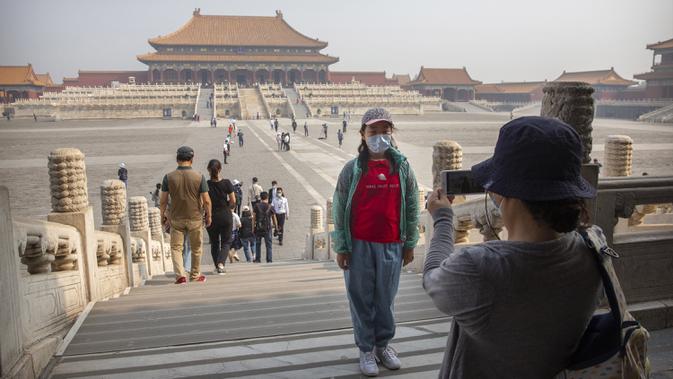 Pengunjung mengenakan masker saat berpose di Kota Terlarang, Beijing, China, Jumat (1/5/2020). Kota Terlarang kembali dibuka setelah ditutup lebih dari tiga bulan karena pandemi virus corona COVID-19. (AP Photo/Mark Schiefelbein)