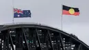 Sebagai informasi, penembakan ini terjadi di tengah aturan ketat pemerintah Australia terkait undang-undang kepemilikan senjata api, terutama sejak tragedi Port Arthur pada 1996. Tampak dalam foto, bendera Australia dan Aborigin dikibarkan setengah tiang di Jembatan Pelabuhan Sydney setelah penembakan di Pantai Bondi, Sydney pada 15 Desember 2025. (DAVID GRAY/AFP)