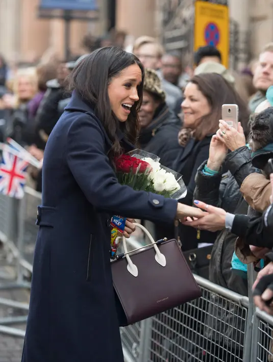 Tunangan Pangeran Harry, Meghan Markle menyapa warga yang menyambutnya pada acara amal memperingati Hari AIDS Sedunia di Nottingham, Jumat (1/12). Meghan Markle menyempurnakan gayanya dengan tote bag Strathbery seharga Rp 8,3 juta. (AP/Alastair Grant)