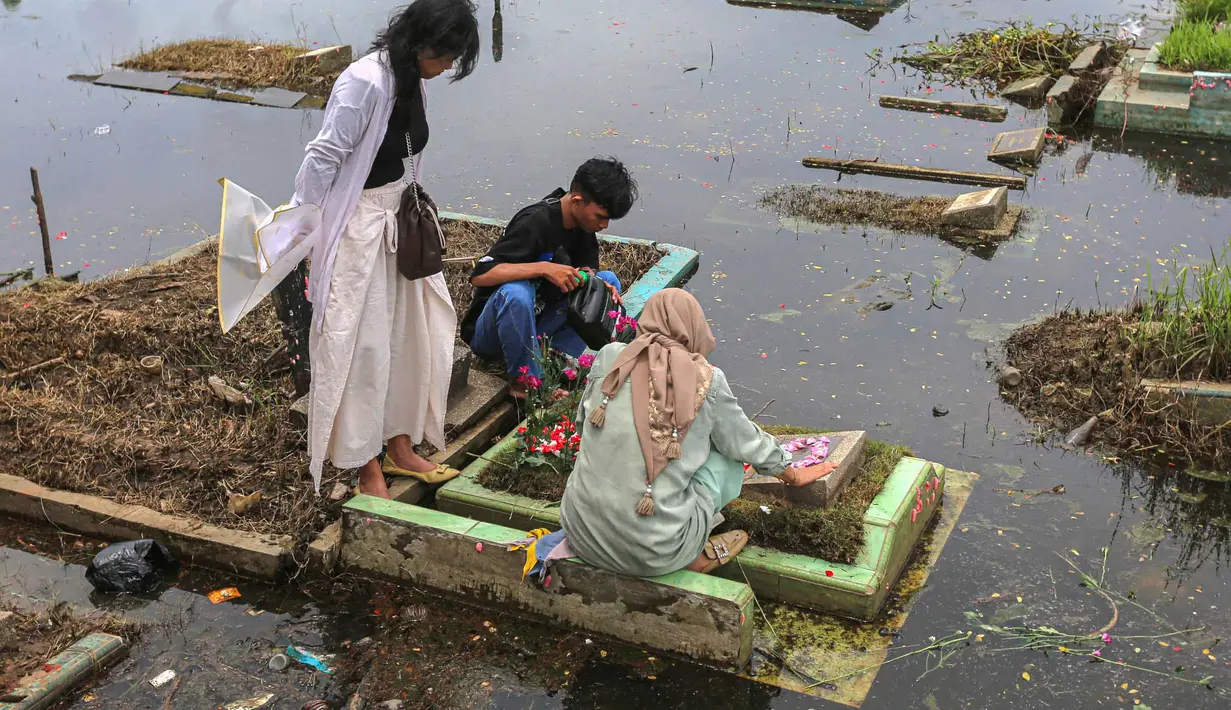 Kondisi cuaca yang kurang bersahabat dan genangan air dengan ketinggian 10 hingga 50 cm tidak menyurutkan niat untuk tetap datang ke lokasi pemakaman untuk mendoakan serta membersihkan area makam keluarga yang telah wafat. Tampak dalam foto, warga mengunjungi makam anggota keluarga mereka di Tempat Pemakaman Umum (TPU) Semper, Cilincing, Jakarta Utara pada 15 Februari 2026. (Syinatria RESPATI/AFP)