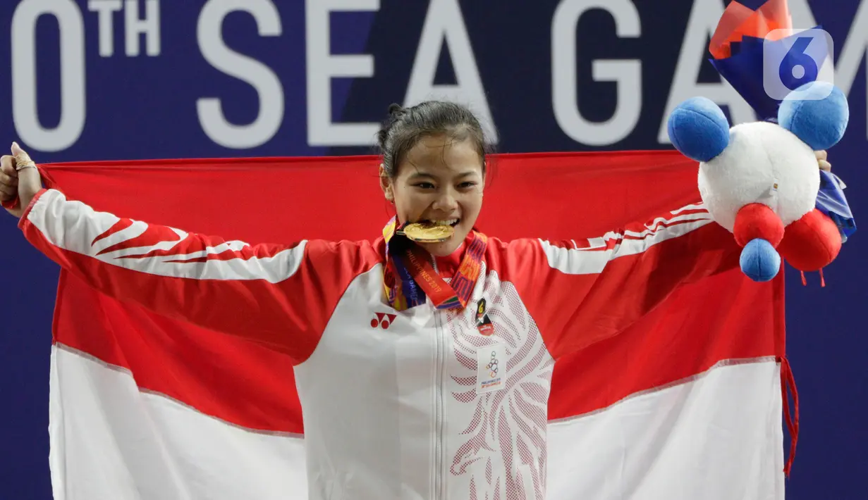 Lifter Windy Aisyah mengibarkan bendera usai mendapatkan medali emas SEA Games 2019 cabang angkat besi nomor 49 kg di Stadion Rizal Memorial, Manila, Minggu (1/12/2019). Windy Aisyah meraih emas dengan total angkatan 104 kg. (Bola.com/M Iqbal Ichsan)