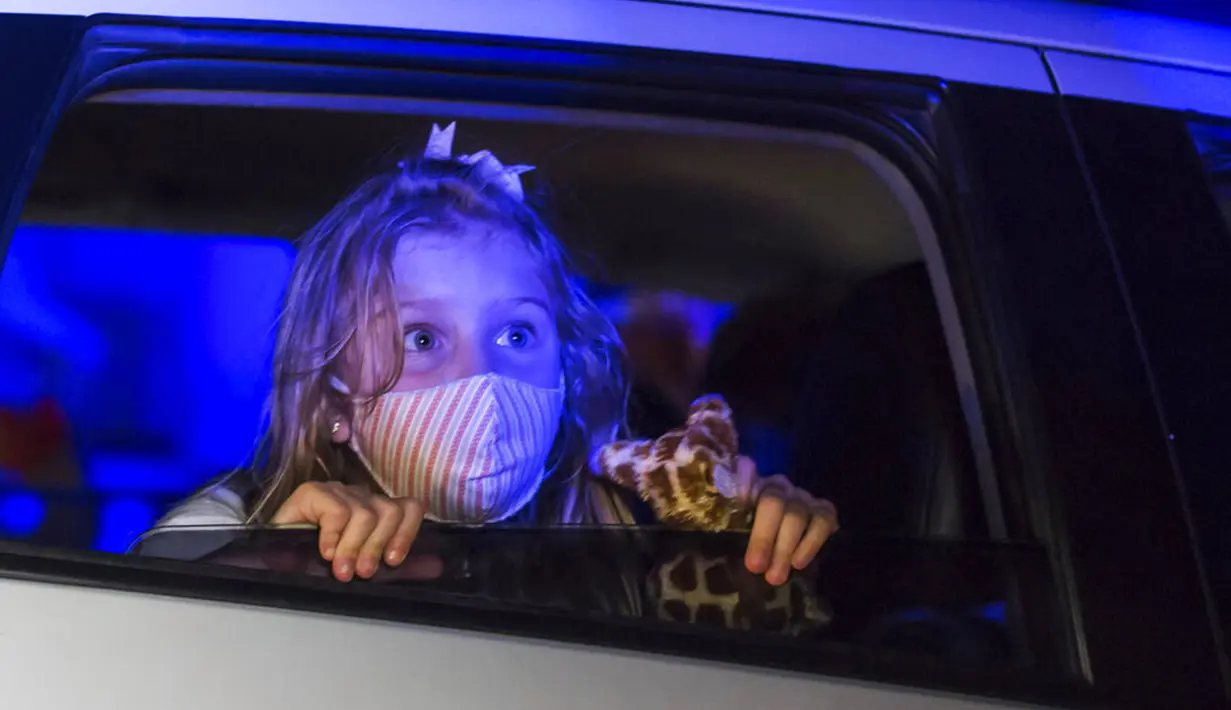 Seorang anak yang mengenakan masker menonton pertunjukan dari dalam mobil di taman hiburan horor Hopi Hari, pinggiran Vinhedo, Sao Paulo, Brasil, Jumat (4/9/2020). Karena pembatasan akibat COVID-19, taman hiburan horor Hopi Hari menampilkan pertunjukan secara drive-thru. (AP Photo/Carla Carniel)