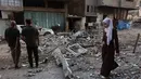 Seorang wanita Palestina berjalan melewati orang-orang yang memeriksa puing-puing bangunan tempat tinggal setelah serangan Israel di Kota Gaza pada Kamis 4 Juni 2026. (Omar AL-QATTAA/AFP)